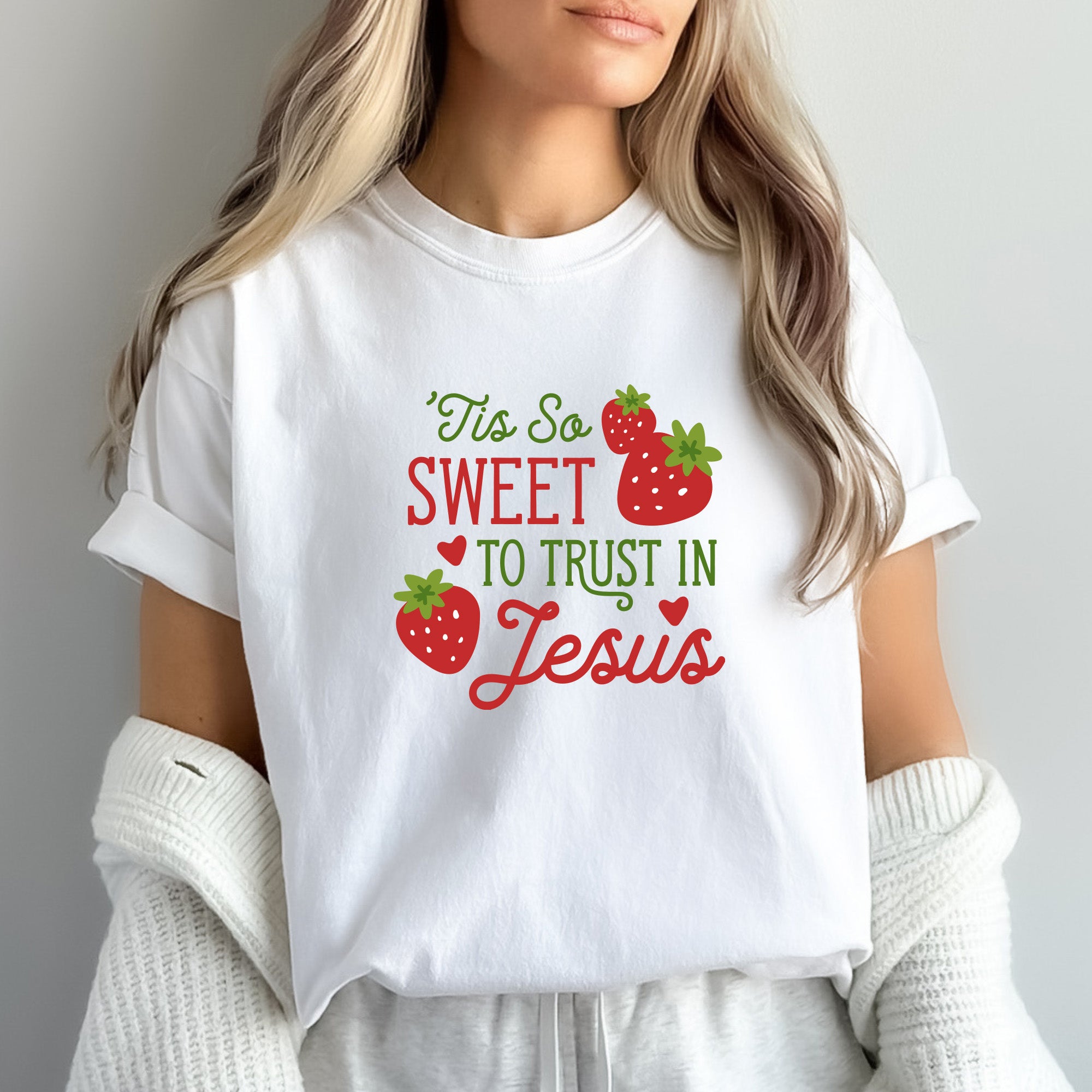 Caucasian woman with blonde hair wearing "Tis So Sweet to Trust in Jesus" shirt in white with red and green text and red strawberries with green stems