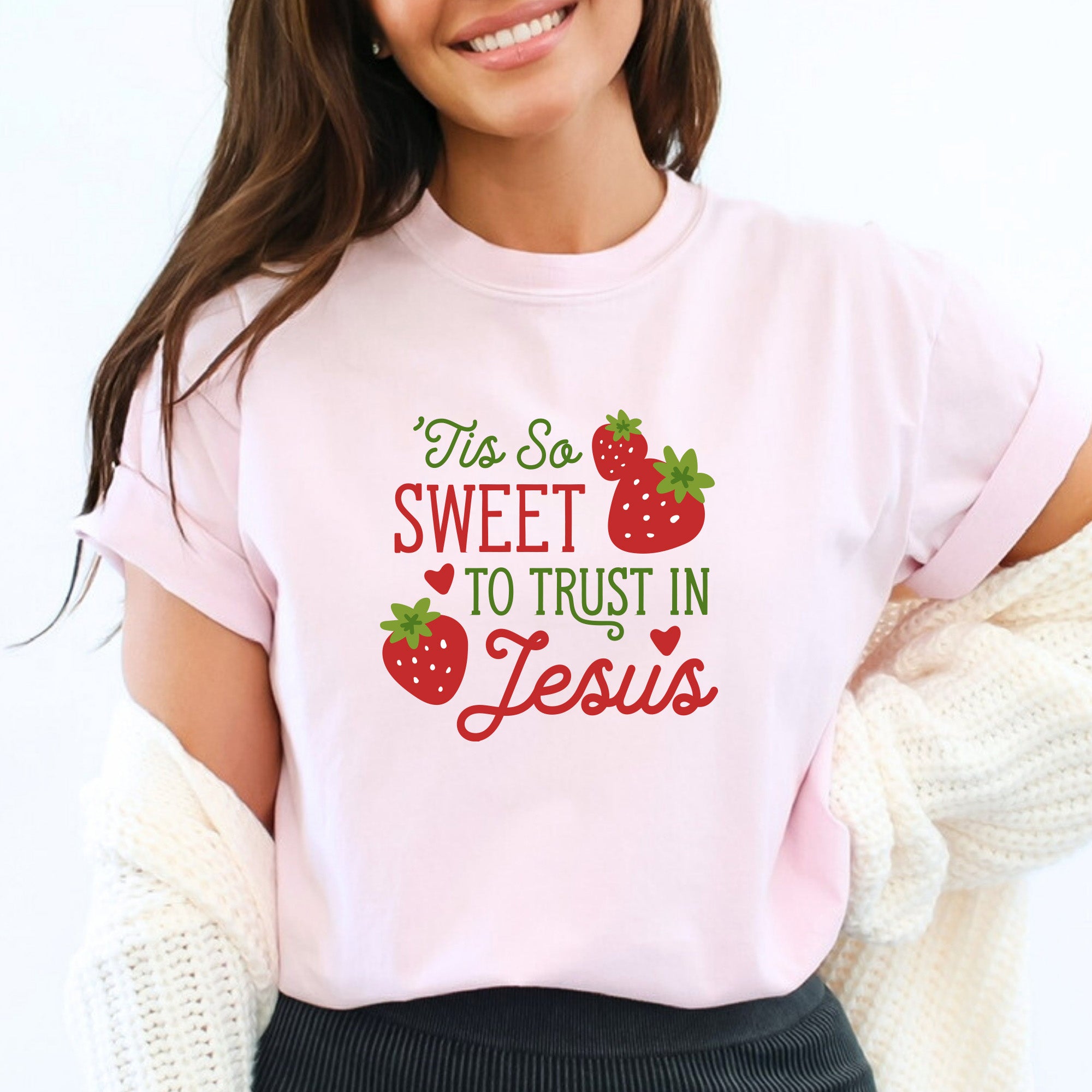 Caucasian woman with brown hair wearing "Tis So Sweet to Trust in Jesus" shirt in blossom pink with red and green text and red strawberries with green stems