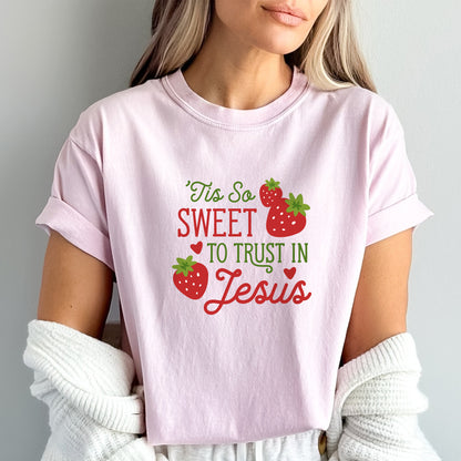 Caucasian woman with blonde hair wearing "Tis So Sweet to Trust in Jesus" shirt in blossom pink with red and green text and red strawberries with green stems